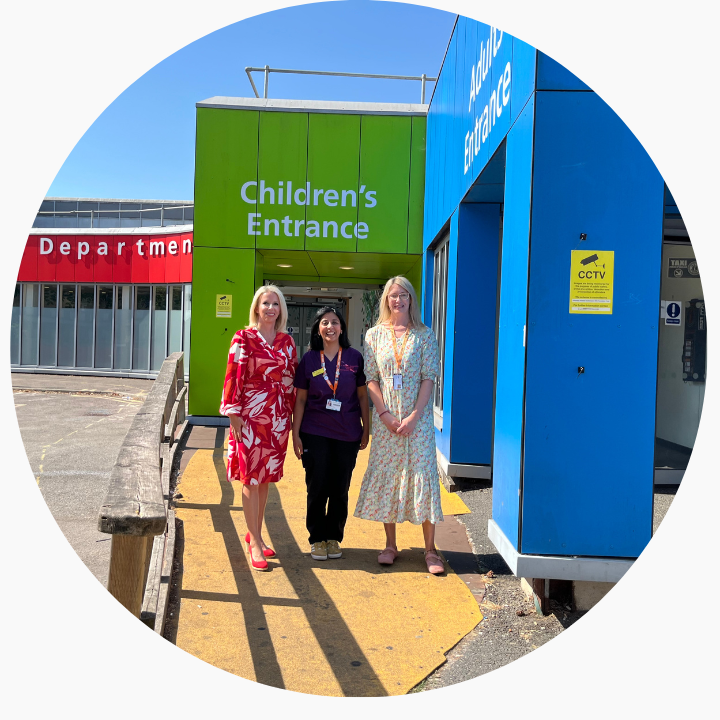 Three women smiling at the camera in front of a green and blue building on a sunny day.